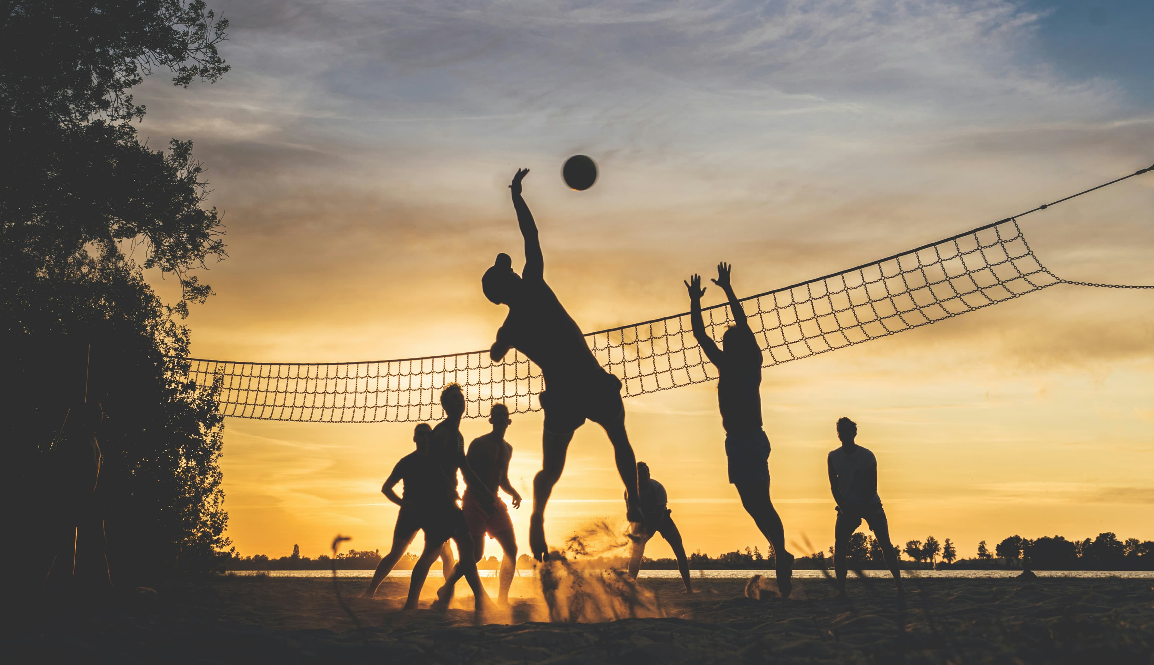 Beach volleyball players silhouetted against a sunset